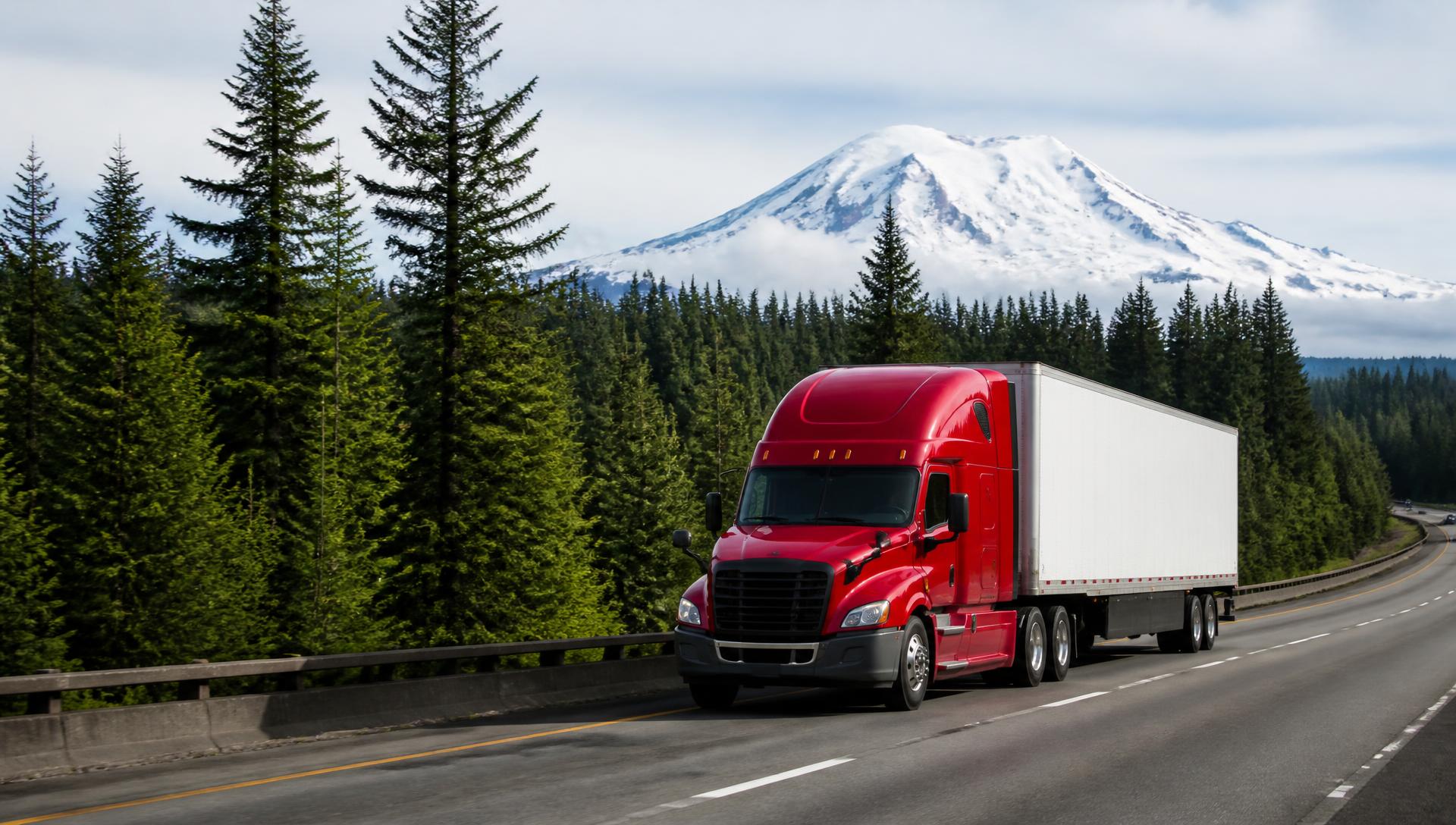 Semi-truck with a dry van trailer traveling an interstate highway through Pacific Northwest evergreen forest